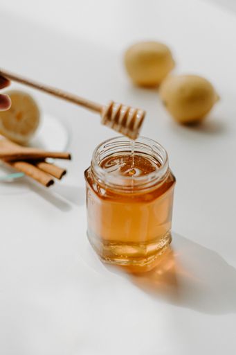 A vertical shot of a hand holding wooden honey dipper stick on a ja