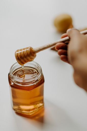 A vertical shot of a hand holding wooden honey dipper stick on a jar