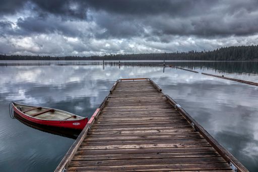 Wooden dock by a lake with a red boat, cloudy sky