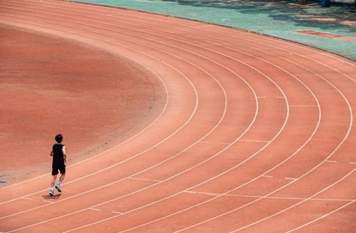 A young student is doing long-distance running exercises on the red track of a university in Wuhan