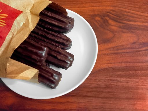 churros covered with chocolate out of their paper bag, traditional Argentine fried dough pastry of Spanish origin, on white background.