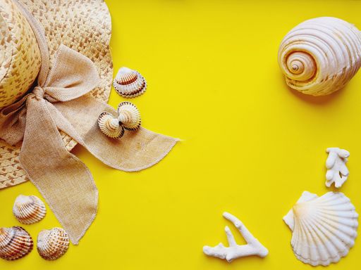 A flat lay with straw hat and sea shells on a yellow background