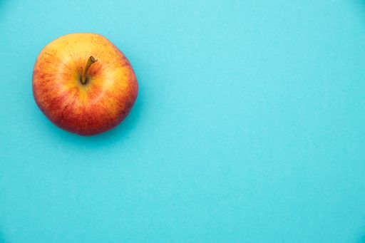 A closeup image of a red and yellow apple in up left corner on a blue background