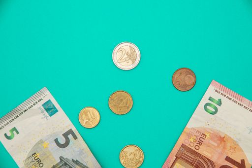A top view of five and ten euro banknotes and coins on a turquoise background