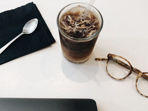 A high angle shot of a coffee near glasses and a laptop on a white platform