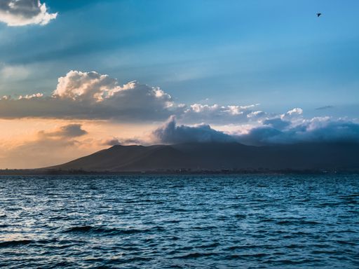 A breathtaking shot of a gorgeous blue sea at sunset with a bird flying over it in a blue and orange cloudy sky