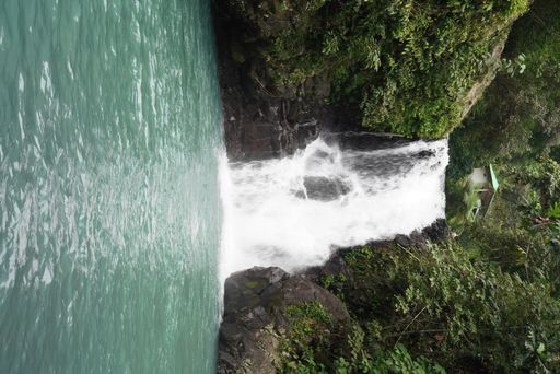 A vertical picture of a waterfall surrounded by rocks covered in greenery in a forest