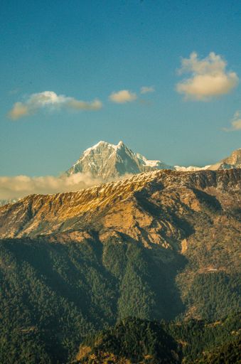 A vertical shot of a scenic mountain peak with snow against a blue sky with a few clouds