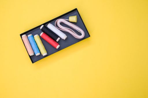 A pack of colorful sewing threads and a measuring tape on yellow background with a copy space
