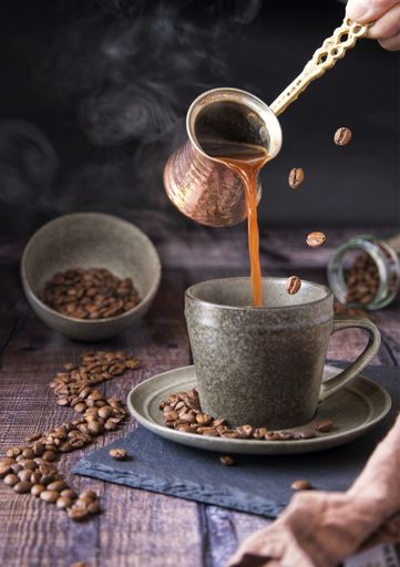 A person pouring coffee into a cup with spilled beans on the table