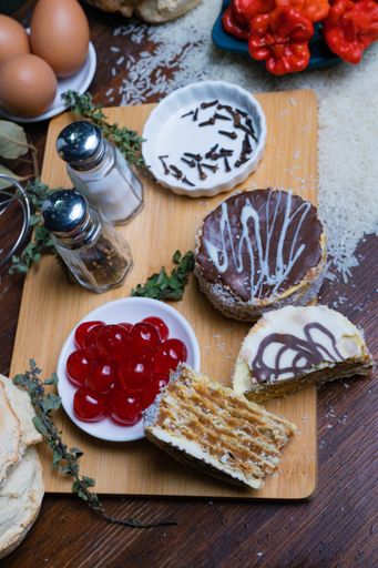 A high-angle shot of cakes with different toppings on the cutting board with baking ingredients
