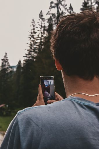 A vertical back view of a male taking a photo of the forest with his phone