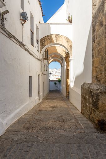 A white building with arches beside a brick walkway and stone steps in Vejer de la Frontera, Spain