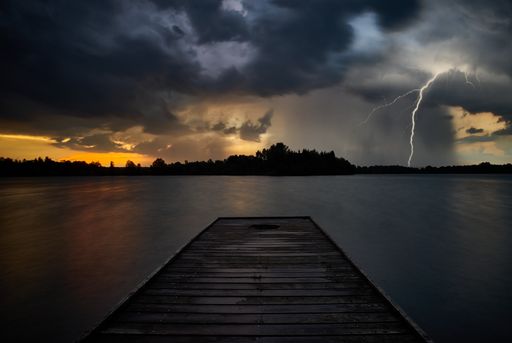 A gorgeous wallpaper with wooden planks leading to the sea and a bolt of lightning in the cloudy sky at dusk
