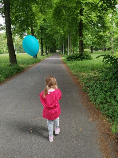 A vertical shot of a preschooler cute girl walking in a park holding a blue balloon