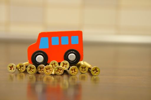 A closeup shot of a wooden toy car and concrete screws on a blurred background