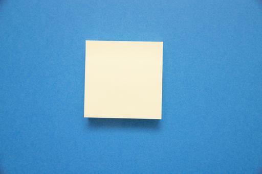 A closeup shot of a white sticky note with space for text isolated on blue background