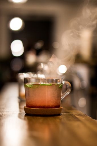 A vertical shot of a glass of herbal tea with a wooden saucer on a blurred background