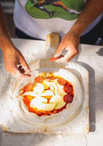 A vertical shot of male hands cooking pizza adding pepperoni