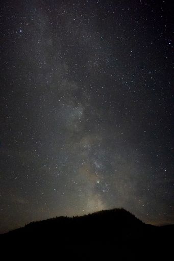 A vertical shot of a hill with a breathtaking scenery of the Milky Way galaxy in the background