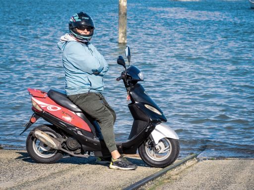 View of man on scooter at the water edge. Auckland, New Zealand - June 21, 2021