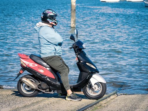 View of man on scooter at the water edge. Auckland, New Zealand - June 21, 2021