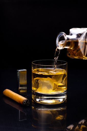 A vertical shot of whiskey pouring into a glass with ice isolated on a black background