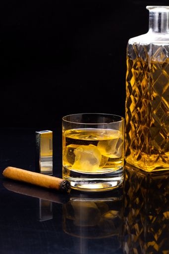 A vertical shot of a glass of whiskey and a cigar on a black background