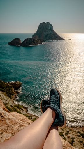 A vertical shot of a person sitting on a rock enjoying the view of Es Vedra in Spain