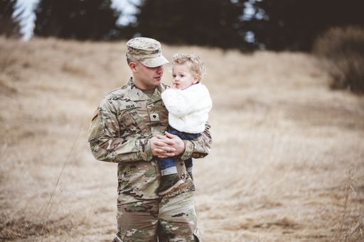 A portrait of a soldier father holding his son in a field