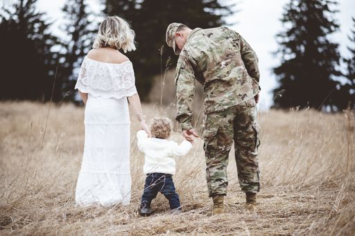 A shallow focus shot of an American soldier and his lovely wife holding their baby's hands while walking on a dry grass field