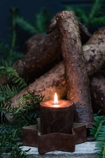 A vertical shot of a burning candle against pine branches and wooden logs for Christmas decorations