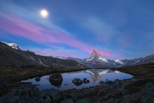 Summer landscape view of the Matterhorn reflecting in the water of the Stellisee lake and the moon setting in a pink coloured sky at dawn