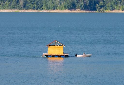 A boat tows a small floating cottage on Lake Bicaz - Romania