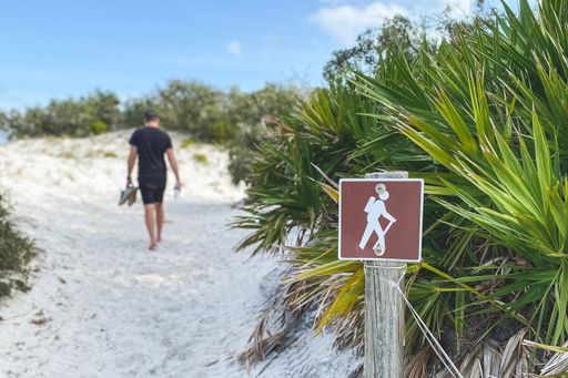A hiking sign on a beach with a man walking on a trail in the background in Gulf Shores, Alabama