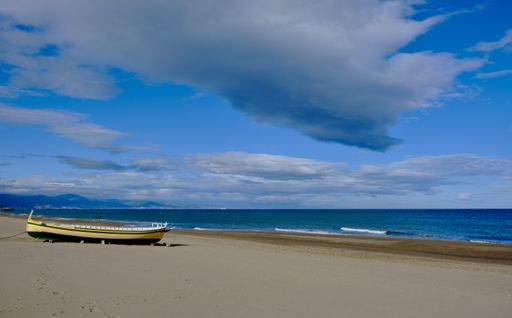 A small rowing boat on the sandy shore at the beach under huge gray-white clouds in the blue sky over the sea