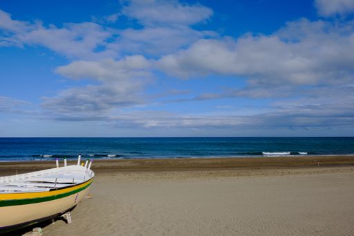 A small rowing boat on the shore at the beach with a bright sky littered with gray clouds over the deep blue sea