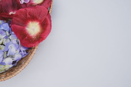 A top view of a basket with red malva and blue hydrangea flowers on a gray surface