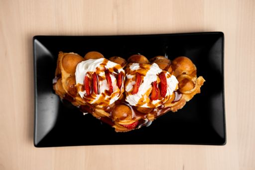 A black plate with wafer cookies, ice cream, and fresh strawberries on a wooden background