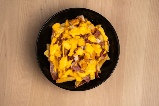 A top view of a black bowl on a wooden table filled with ham and cheese