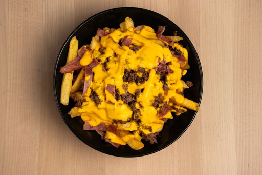 A top view of a black bowl on a wooden table filled with ham and cheese