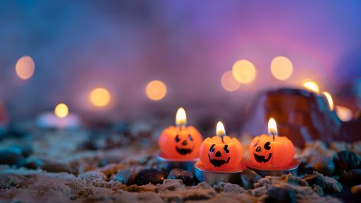 Halloween background, 3 pumpkin shaped candles in the foreground against an out of focus background with yellow lights