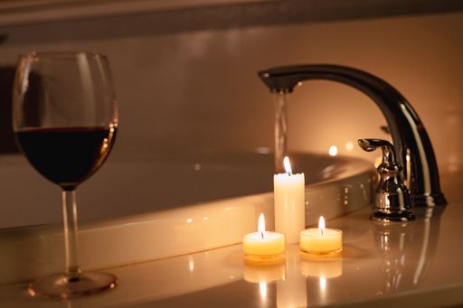 Three illuminated candles beside a bottle of wine on a countertop