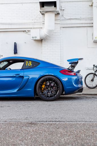 A vertical shot of a beautiful blue Porsche 981 Cayman GT4 race car parked on a side street