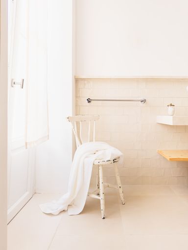 A boho style bathroom bathed in soft day light with a wooden vintage stool