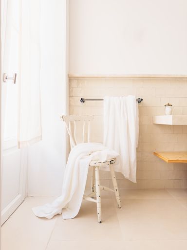 A boho style bathroom bathed in soft day light with a wooden vintage stool