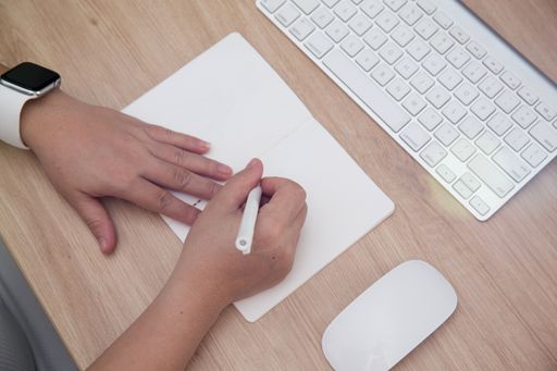 An overhead shot of female hands writing in notebook and a keyboard on the table