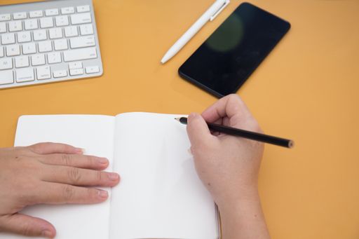 An overhead shot of female hands writing in notebook and a keyboard on the table
