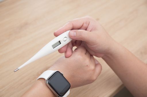 A high angle shot of female hands with thermometer and a smartwatch