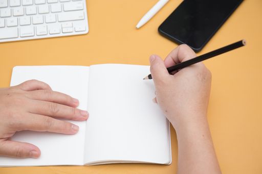 A high angle shot of female hands writing in notebook and a keyboard on the table